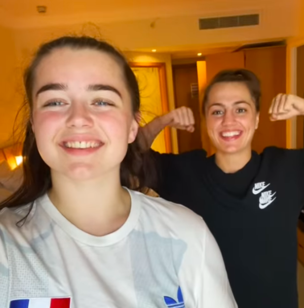 Two women flexing their biceps in a hotel room.