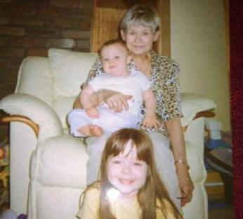 Photo of a grandmother with two grandchildren sitting on a cream-colored recliner.