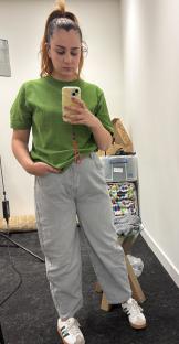 Woman in green shirt and gray jeans taking a selfie.