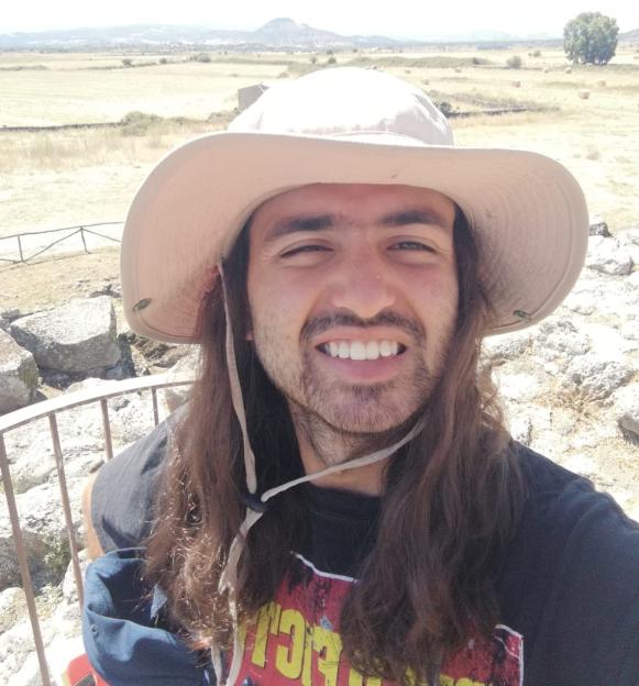 Selfie of a smiling man with long hair wearing a sun hat, taken outdoors.