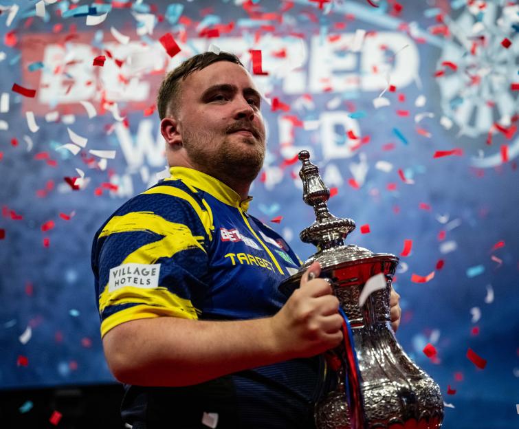 Luke Littler holding a trophy, confetti falling.
