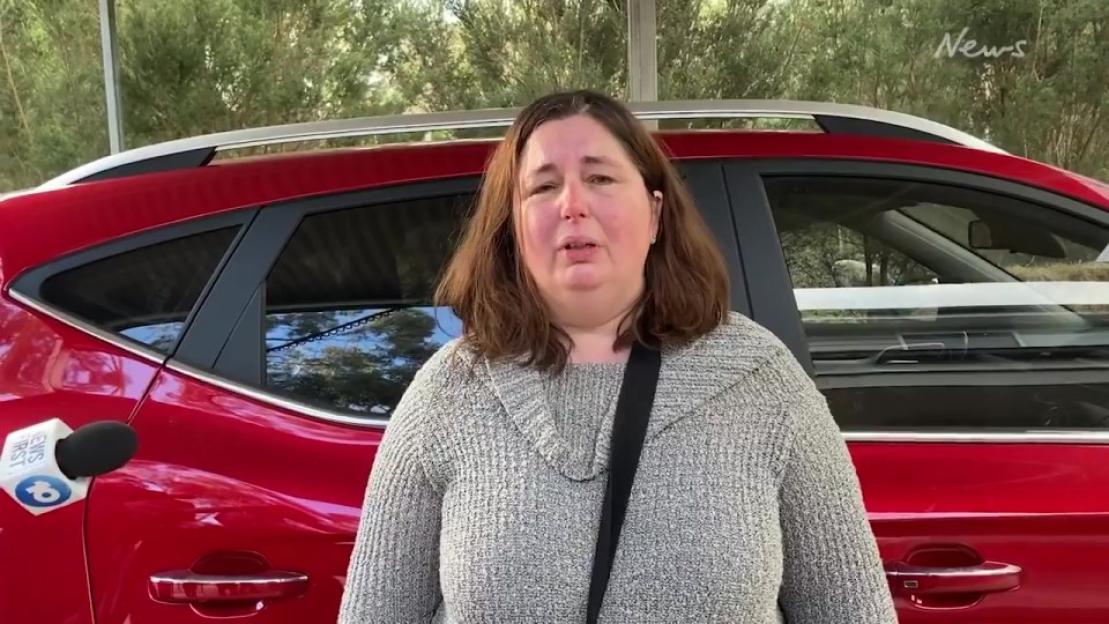 Woman being interviewed in front of a red car.
