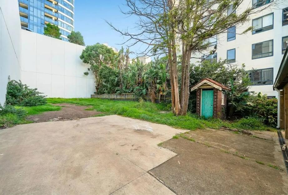 Backyard of residential property with small shed and building in background.