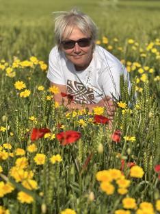 Woman in sunglasses crouching in a field of yellow and red flowers.
