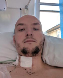 Bald man in hospital bed with neck dressing.