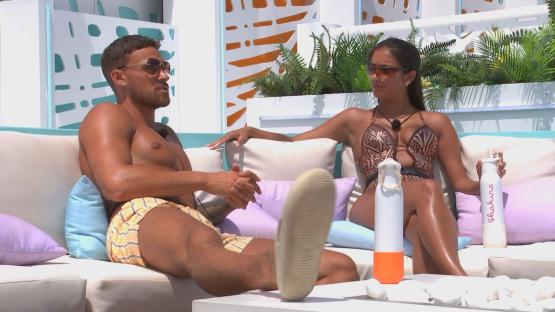 Two Love Island contestants sitting on a couch and talking.