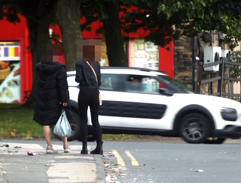 Two people walking on a sidewalk near a street with a car driving by.