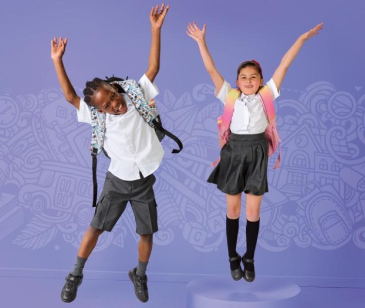 Two children in school uniforms joyfully jump in front of a whimsical background.