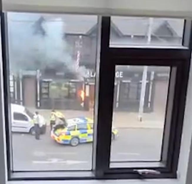 View from a window of a street scene with a small fire, police officers, and police cars.