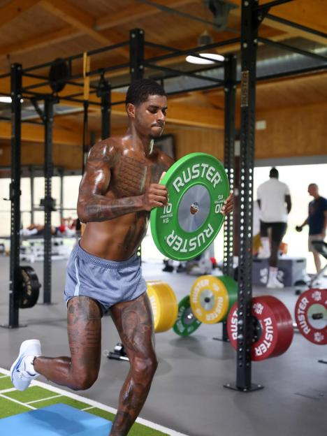 Man with tattoos lifting weights in a gym.