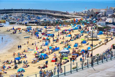 Crowded beach in Lyme Regis, UK, with people sunbathing and swimming.
