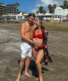 Pregnant woman and man on beach.