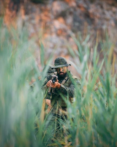 Soldier aiming a rifle while hidden in tall grass.