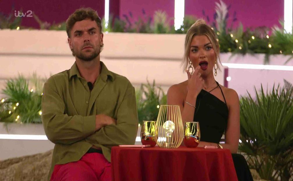 A man and a woman sit at a table, looking surprised.