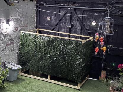 Artificial hedge privacy screen attached to a wooden frame.