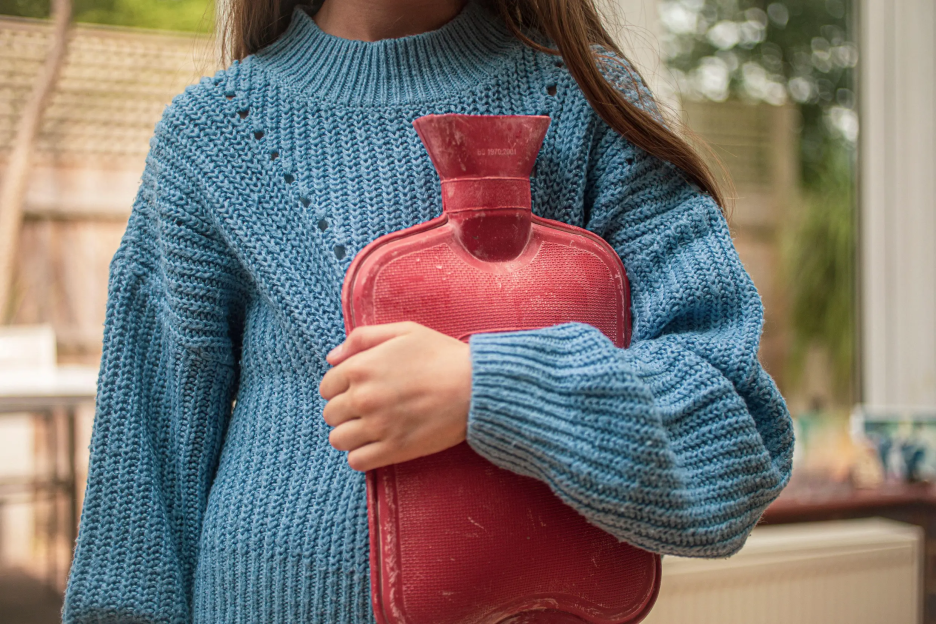 A person in a blue sweater holding a red hot water bottle.