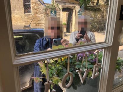 Reflection of two tourists taking selfies in front of a window decorated with a