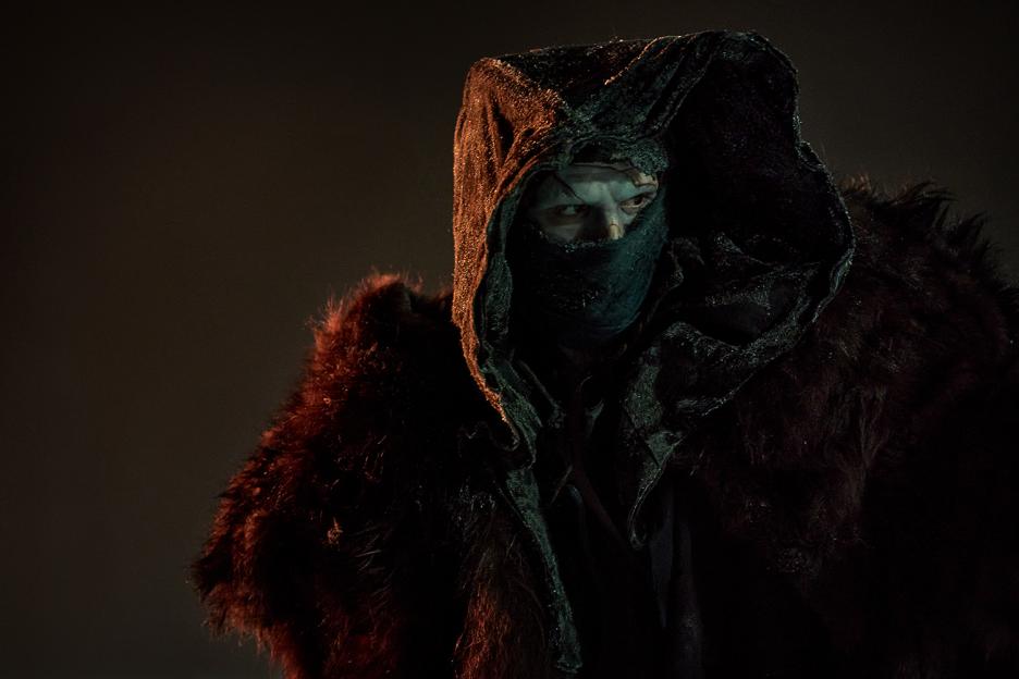 Jacob Elordi as the Creature in Frankenstein, wearing a dark hooded cloak and fur.