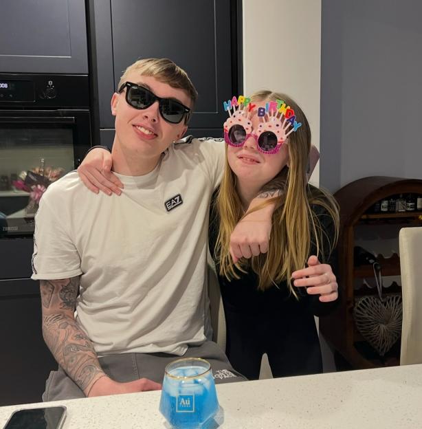 Brother and sister posing together; the girl is wearing birthday glasses.