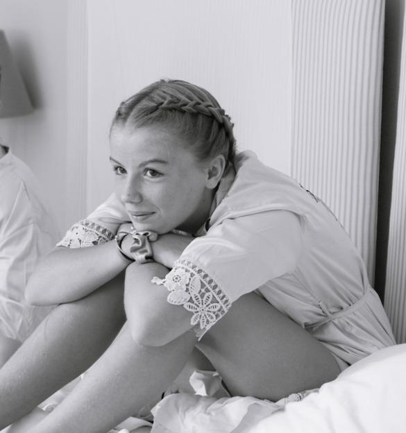 Black and white photo of a teenage girl sitting on a bed, arms wrapped around her knees.