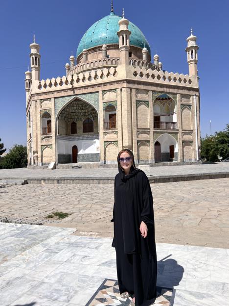 Woman in black abaya standing in front of a mosque in Afghanistan.
