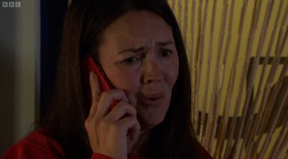 Screenshot of a woman with long brown hair, wearing a red shirt, looking distressed while talking on a red phone.
