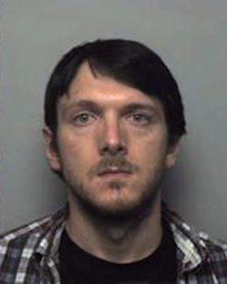 Mugshot of a man with dark hair and a plaid shirt.