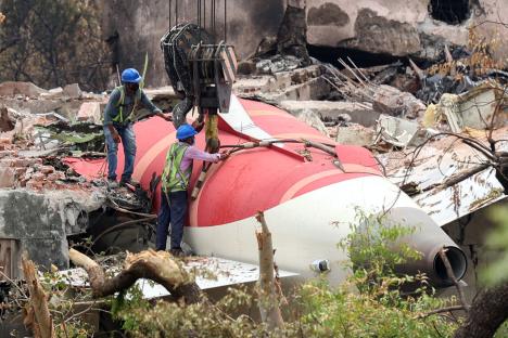 Workers removing wreckage of an Air India plane using a crane.