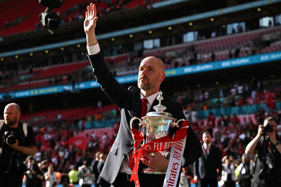 Erik ten Hag holding the FA Cup trophy and waving to fans.