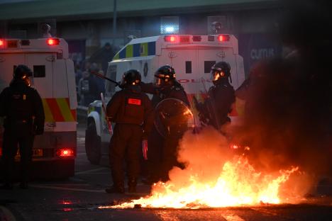 Riot police in Ballymena, Northern Ireland, face a burning vehicle during a protest.