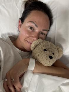 Woman in hospital bed holding teddy bear.