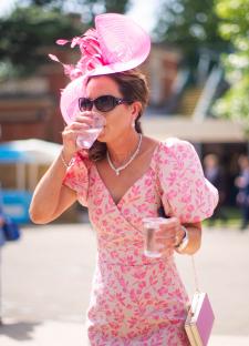 Woman in pink floral dress and hat drinking water.