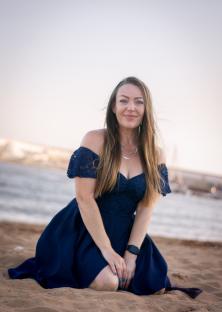 Woman in a blue dress kneeling on a sandy beach.