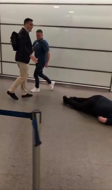 A man lying on the ground at St. Pancras railway station while two men stand nearby.