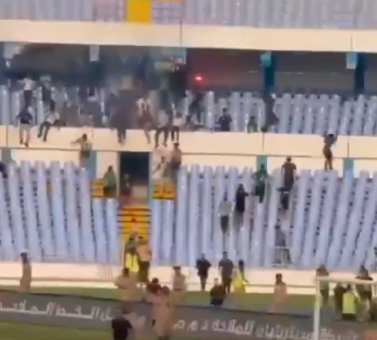 People climbing over barriers at a stadium.