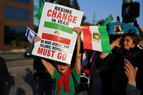 Protestor holding Israeli and pre-Islamic Republic Iranian flags and a sign that reads