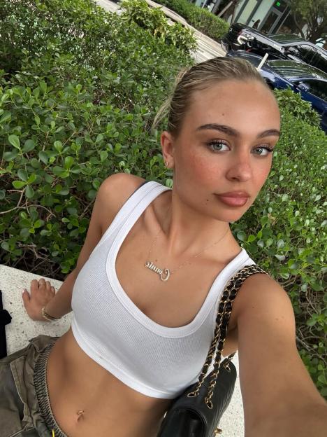 Woman wearing a white tank top and gold necklace.