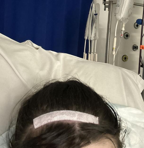 Woman in hospital bed with bandage on forehead.