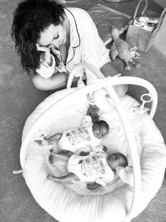 Black and white photo of a woman sitting on the floor next to a baby playmat containing her twin babies.