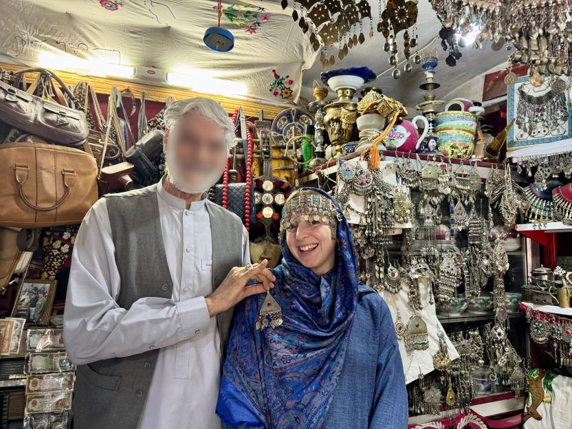 Woman in blue headscarf smiles with man in shop surrounded by jewelry.