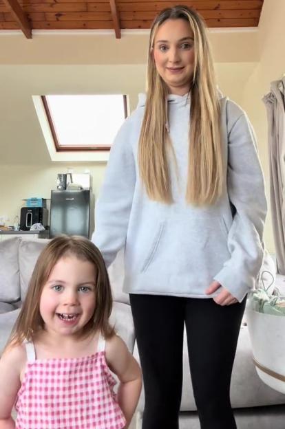 A woman and young girl stand together indoors.