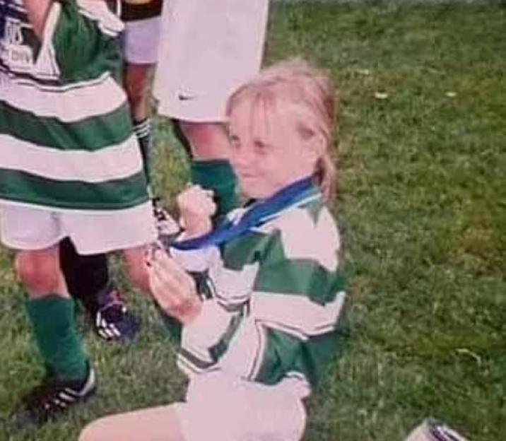 Young girl in soccer uniform holding a medal.