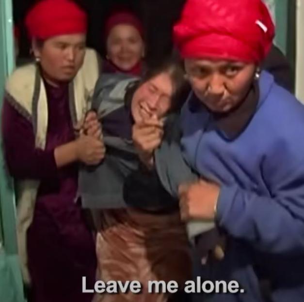 A distraught woman being forcibly held by several other women. The text