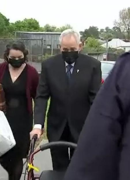 Man in suit using a walker with a woman beside him.