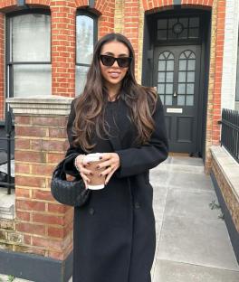Woman in black coat holding coffee cup.