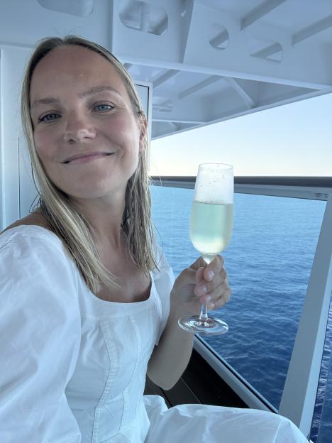 Woman in white dress enjoying champagne on a ship's balcony overlooking the ocean.