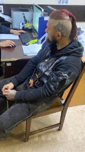 A man with a wolf tattoo sits in a chair at a police station.