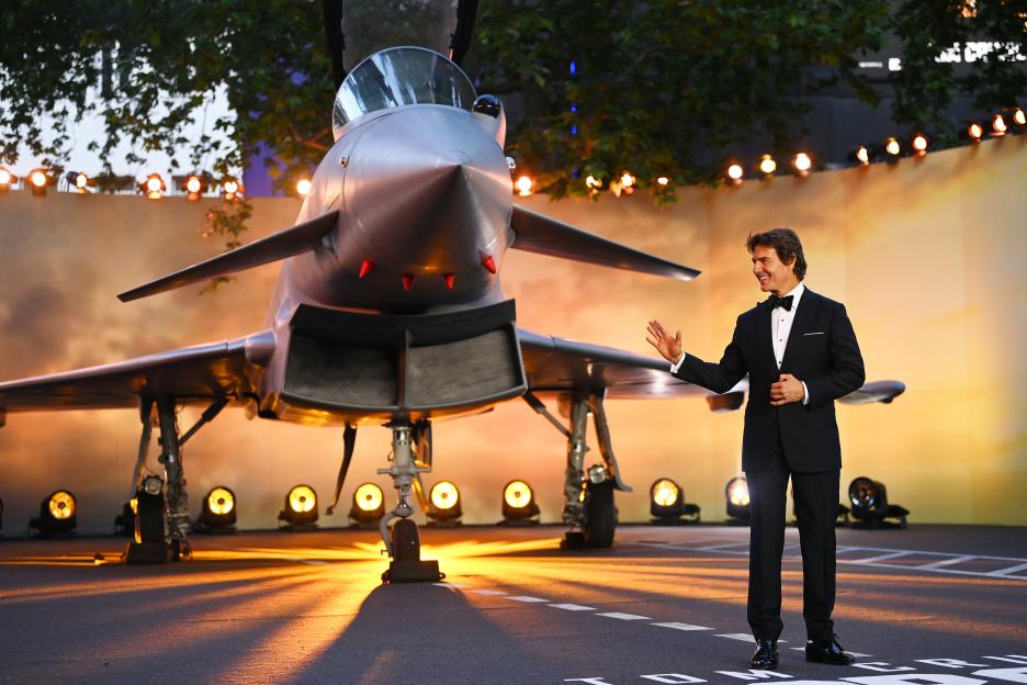 Tom Cruise at the Top Gun: Maverick premiere, standing in front of a fighter jet.