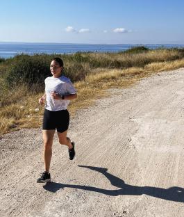 Woman jogging on a dirt road near the ocean.