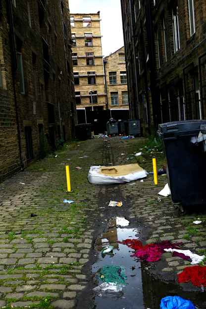 Littered alleyway between brick buildings.